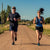 A man and a woman running side by side on a dirt road.