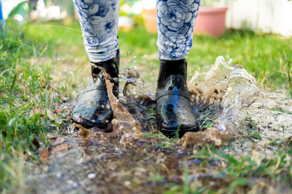 A woman wearing Gracie rain boots while splashing in a puddle of water