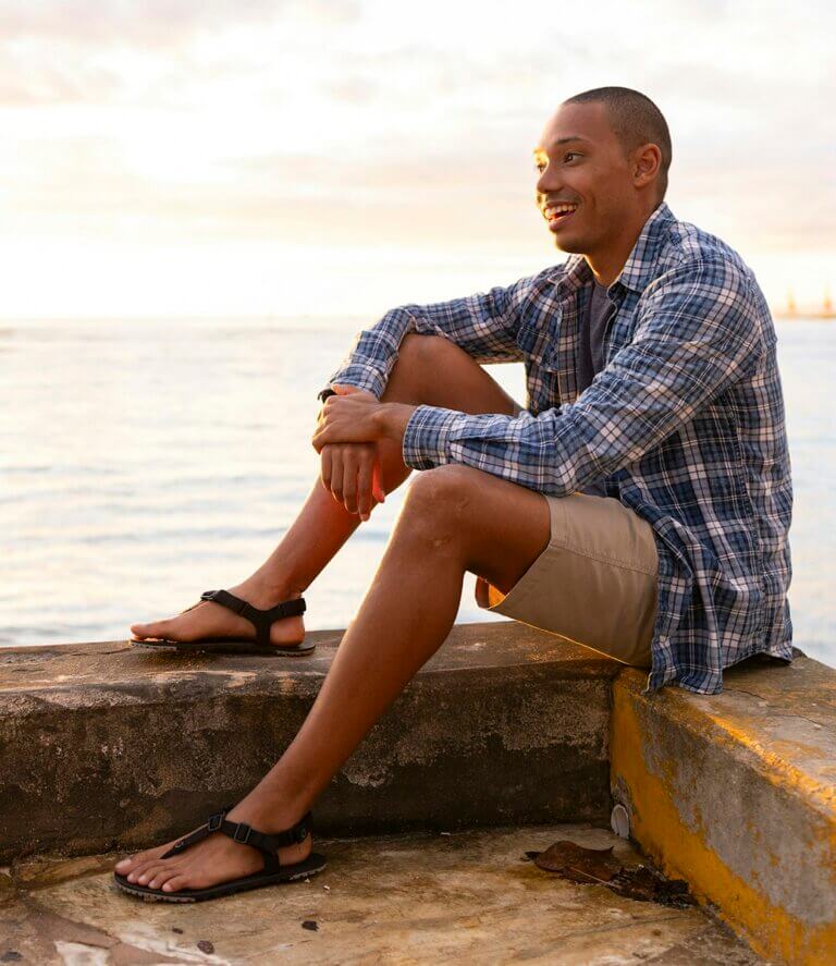 A man smiling and sitting on the water with his H-Trail sandals