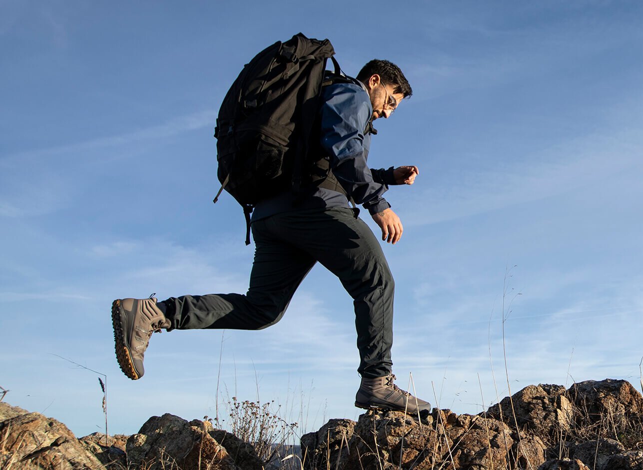A man wearing Scrambler Mid II boots leaping from one rock to another outside on a hike