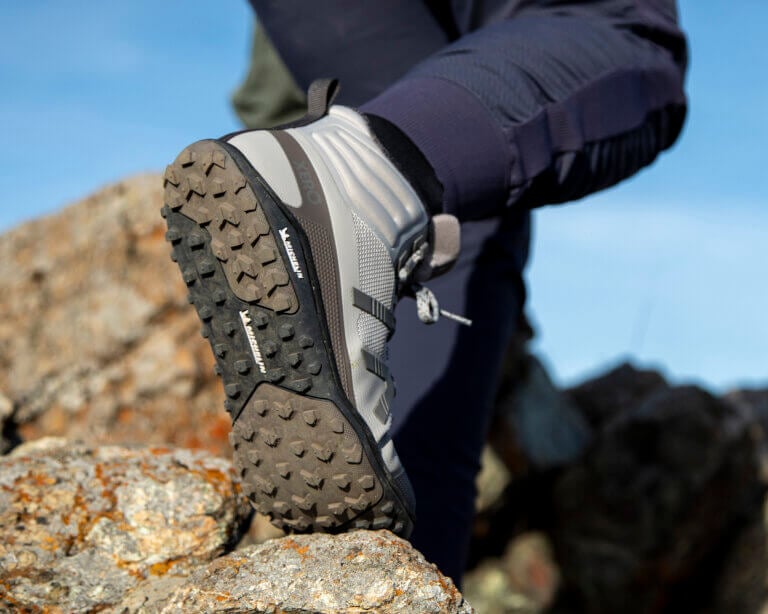 A close up shot of a woman wearing Scrambler Mid II boots showing off their flexible Michelin sole with a large step down