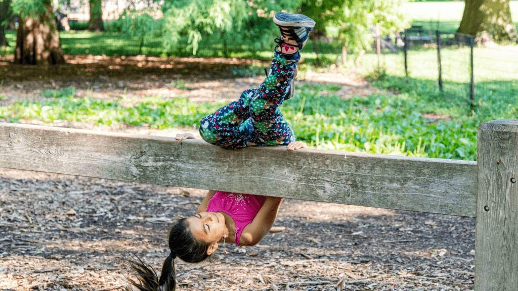 A kid hanging onto and sliding under a wooden bean while doing parkour