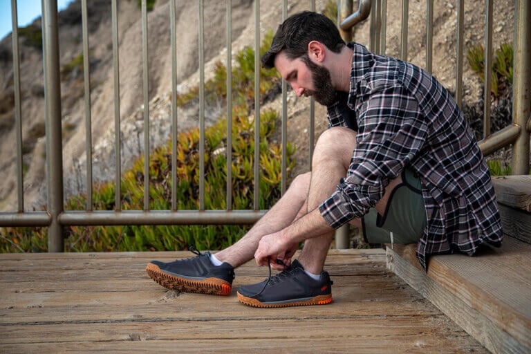 A man sitting outside on a wooden deck lacing up his Ridgeway Mesh Low shoes