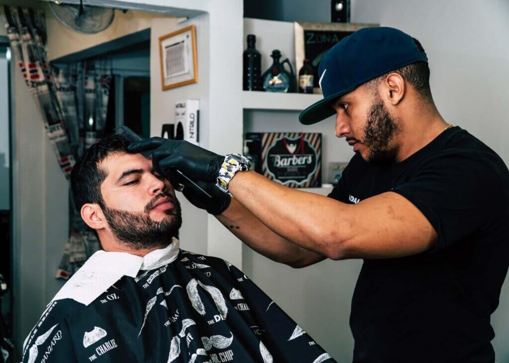 A barber cutting a man's hair while wearing a hat and gloves