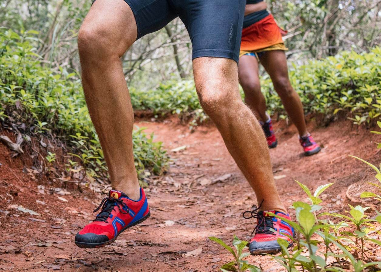 Two people running down a dirt trail in bright red and blue Xero Shoes