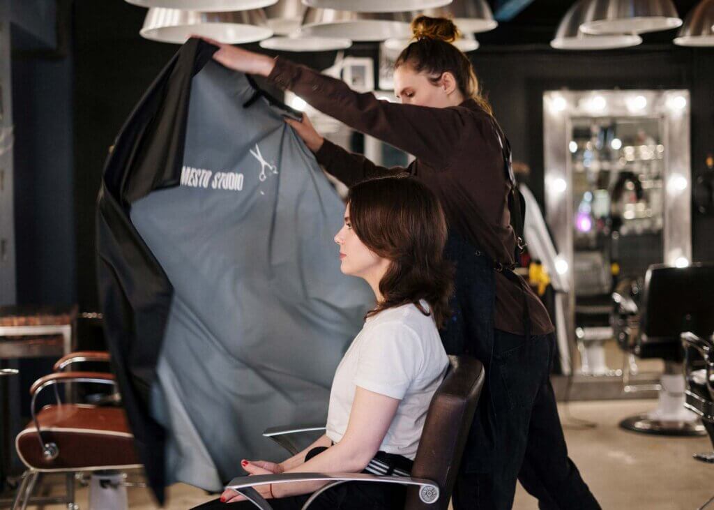 A barber dramatically throwing on an apron onto a woman about to get a haircut