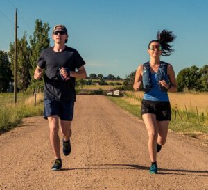 A man and a woman running side by side on a dirt road.