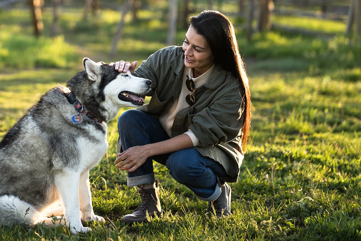 A woman petting her dog outside in a grassy park while wearing her Breckenridge boots