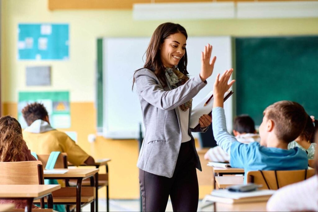 A professional looking young teacher high-fiving a student in the classroom