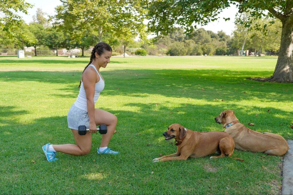 Women doing a lunge in front of her dogs at a park wearing blue xeroshoes prios