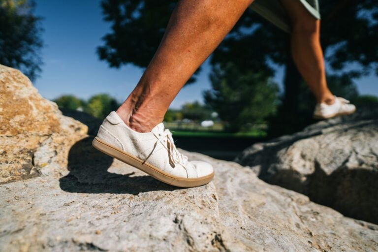 A person walking across some rocks wearing his Dillon Canvas shoes.