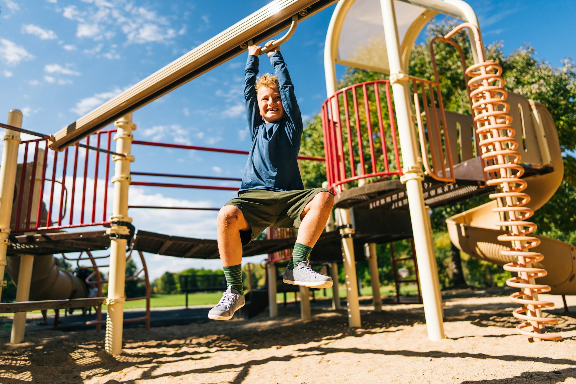 A kid playing on the playground hanging onto the track ride wearing his Dillon - Big Kids shoes.