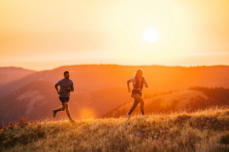 A couple running across a grassy hill while the sun is setting in their Scrambler Low EV shoes.