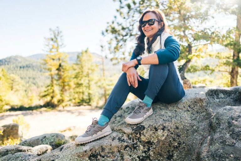 A smiling woman sitting on a rock while hiking a mountain wearing her Scrambler Trail Low WP.